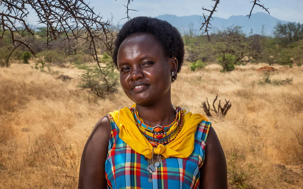 Nancy, a former sponsored child, is standing outside a field wearing a colourful dress. 