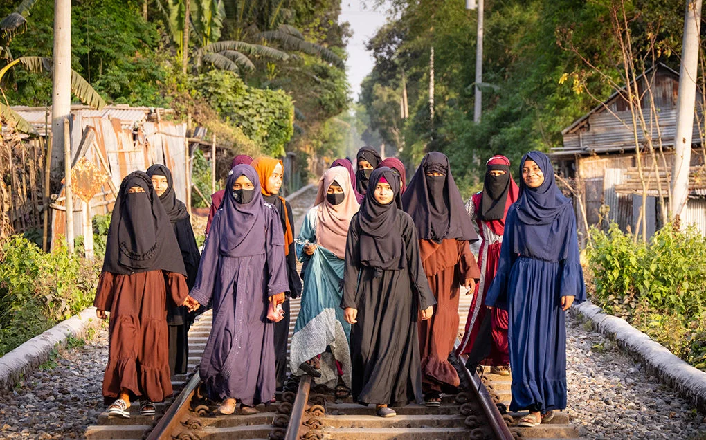 A group of Bangladeshi girls, wearing hijabs and niqabs, walk together on a path.