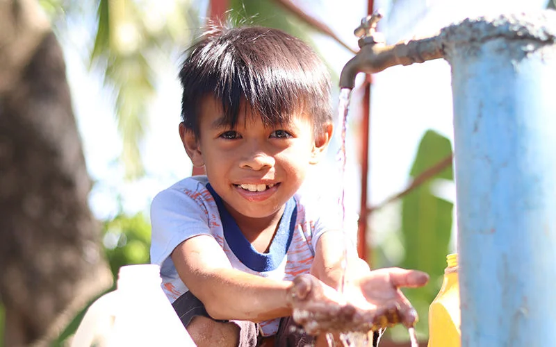 Jory smiles brightly as he washes his hands in with tap water. Siayan, Philippines.